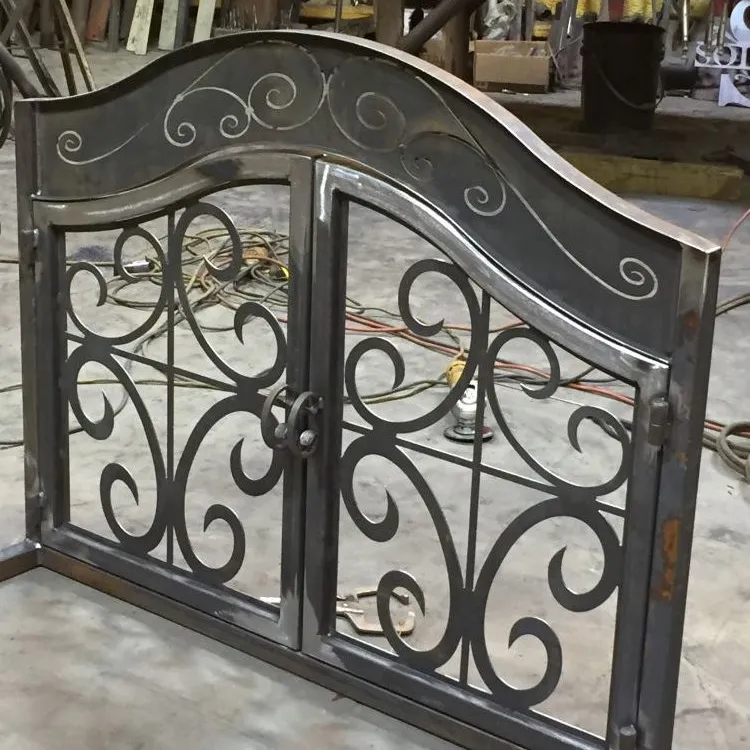 A double-leaf arched courtyard gate in raw burnished steel, both leaves filled with curling formed scrollwork and the arched header scribed with matching scroll lines, standing on the fabrication shop floor.