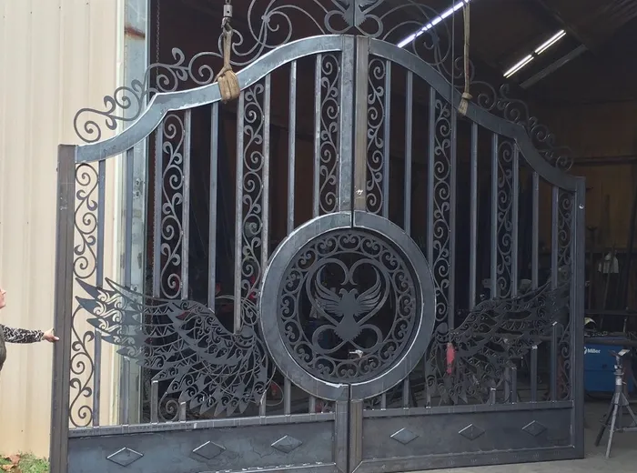 Both leaves in bare steel, slung from chain hoists in the open shop doorway, the winged medallion and the swept wings already fitted.