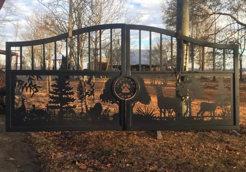 The Tennessee Deer Gate shut across a field entrance in low sun, bare trees and a metal barn showing through the cut woodland scene, with a utility pole standing in front of the right leaf.