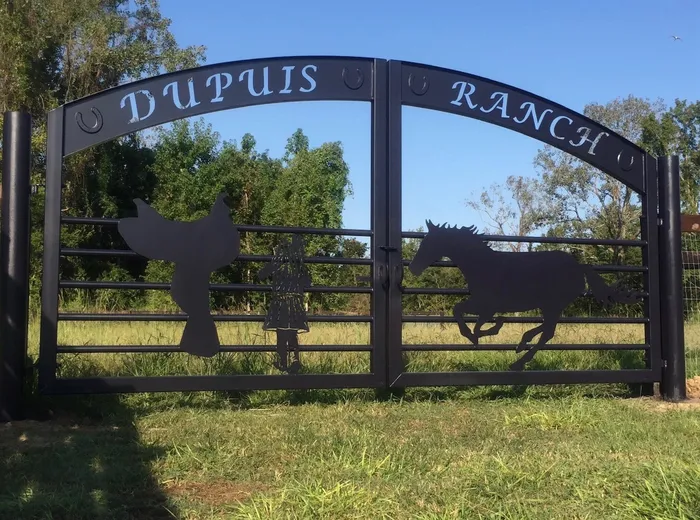 The same gate from the left in low evening sun, the cut lettering of the arched band and the black posts standing against a clear blue sky.