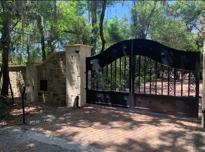 The Tampa Gate closed across a paver drive between cut-stone columns, its wave-topped black leaves studded along the rails, under live oaks hung with Spanish moss.