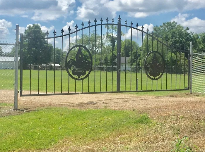 The MCA Gate under a blue sky, both circular fleur-de-lis medallions visible against the open field behind.