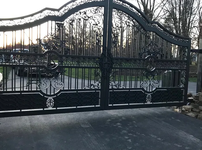 The gate from the side at sunset, the two leaves meeting at a round rosette on the mid-belt, with lawn and the drive showing through the pickets.