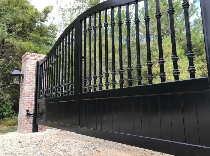 Close oblique view along the Kling Gate, the stacked collars on each baluster stepping down with the curve of the top rail above the ribbed lower panel, with a brick pillar and lantern at left.