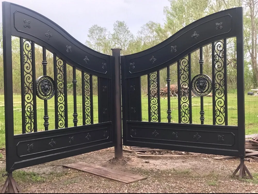 Both leaves of the New Yorker Gate hung on a bare steel post in a grassy yard and angled toward the camera, their gloss black rosettes, scrollwork and lion's-head rings bright under an overcast sky.