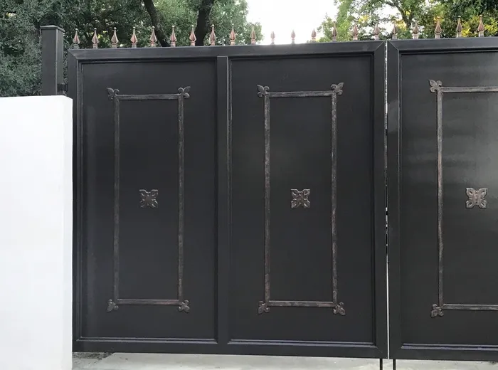 Close view along the Dallas Estate Gate, two of the four panels full in frame and the applied frames standing proud of the sheet with fleur-de-lis at each corner and a rosette at the centre.