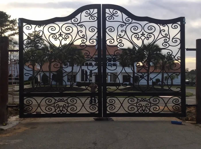 The Inman Gate at dusk, the scrollwork reading as silhouette against a pale sky with the drive and house beyond.
