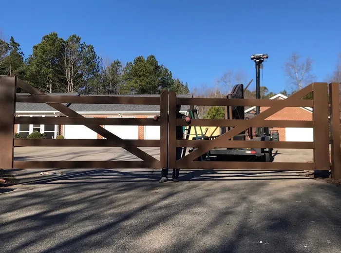 The Virginia Farm Gate on installation day, both leaves closed and held at the centre, with a ladder and trailer standing on the drive beyond.