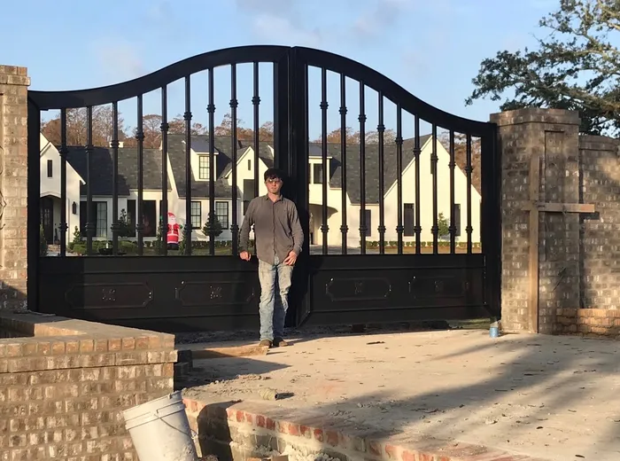A man standing at the closed centre joint of the Fresina Gate, giving the leaves their scale, with the house, brick piers and an unfinished drive around him.
