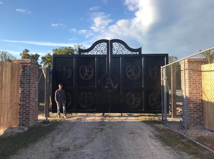 Square-on view from down the gravel drive, the gates set between brick columns with the openwork scroll of the arch bright against the sky.