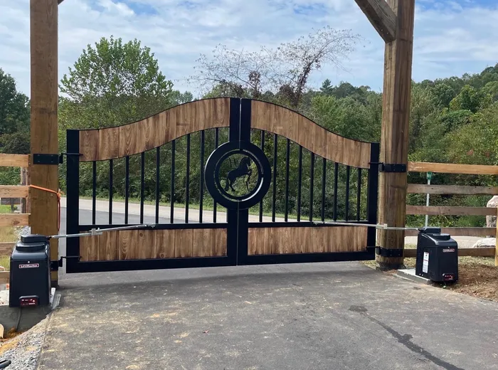 The same design straight on under a timber frame, the ring at the centre joint holding a rearing horse cut from plate, with woods and a paved drive behind.