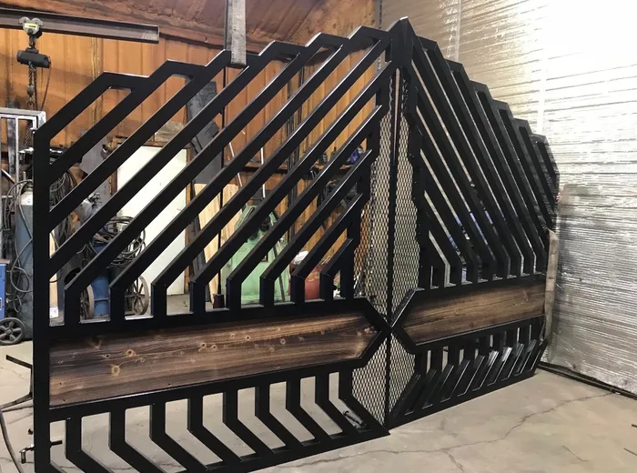 Both leaves standing finished in the shop against a timber wall, a chain hoist and welding gear behind them, the stepped diagonal pattern visible end to end.
