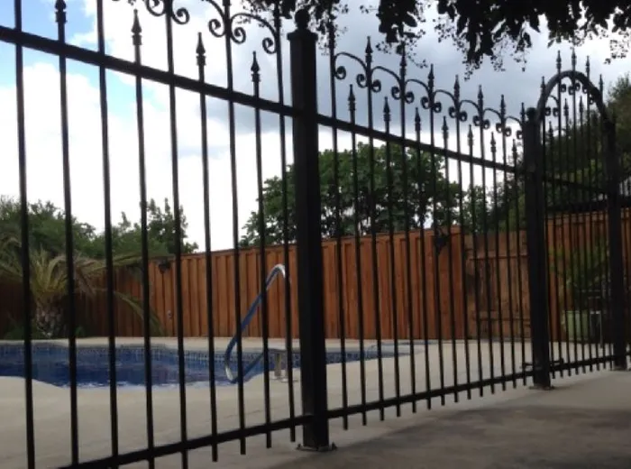 The iron pool fence running along the wood privacy fence line, pickets evenly spaced against the sky.