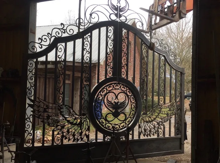 The finished black gate held upright in the shop doorway, its scrollwork reading against a brick house and bare winter trees outside.