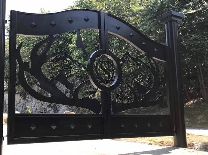 The Wilderness Gate close and from the left, the antler-wreathed monogram medallion at the centre and the pyramid studs along the curved top band catching the light.
