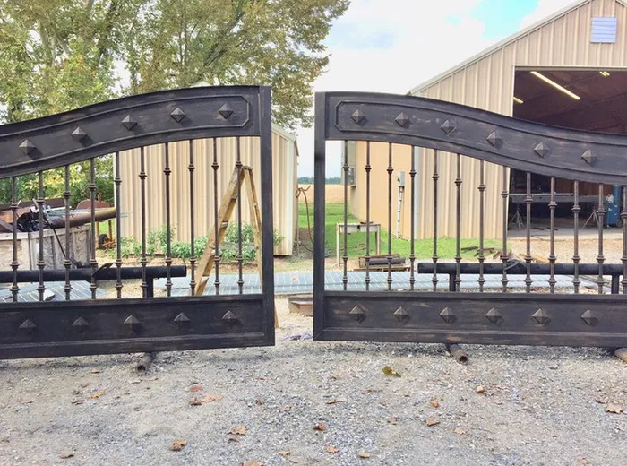 Both leaves standing loose in the gravel yard outside the workshop, resting on lengths of pipe, with the studded S-curve rails and turned balusters close to the camera.