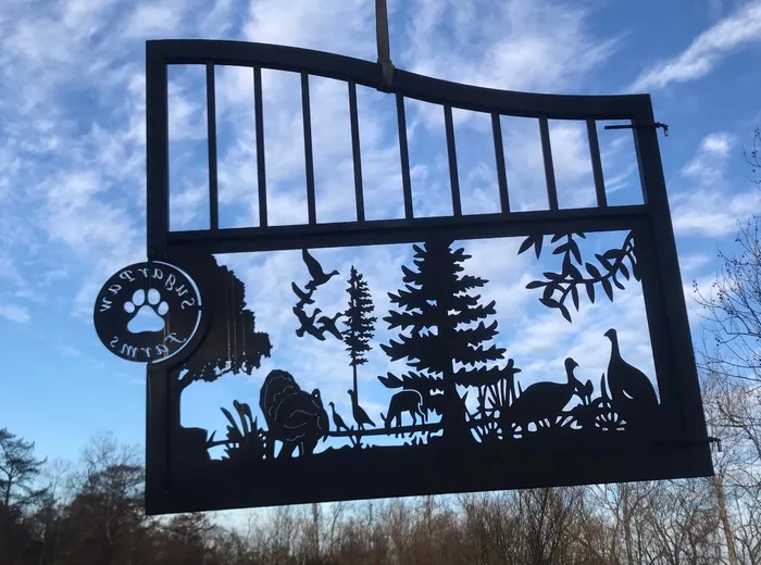 The other leaf lifted against the sky and seen from the back, so the lettering around the paw-print medallion reads in reverse, with pines, ducks lifting, ground birds and grasses in the cut panel.