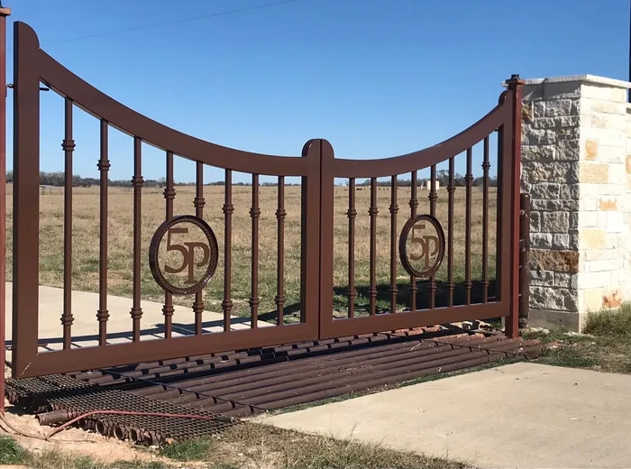 The 5P Gate from the side of the drive, both monograms in line, a stacked-stone column at the hinge and a grid of steel pipe set into the entrance.
