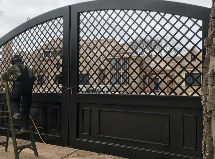 The hung gate seen at an angle from the left, the arc of the top rail falling away and the raised panels of the lower half reading dark against the graded dirt of the drive, a tree trunk close at the right edge.