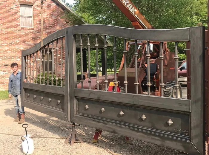 Both leaves in bare steel outside the shop, propped on stands beside a brick building while a worker steadies the left one, the arch continuous across the pair.