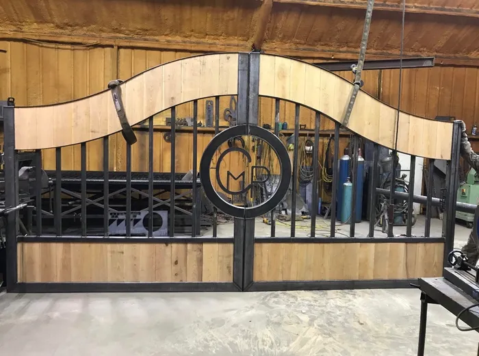 Both leaves standing inside the shop before finishing, the frame still bare steel and the boards fresh, with the monogram ring welded across the joint.