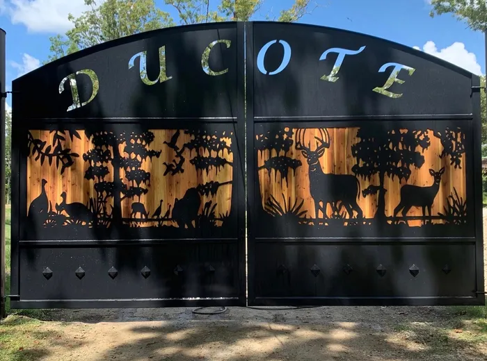 The gate with tree shadows falling across it and leaves down on the drive, the timber boarding behind the pierced scene showing warm against the black steel.