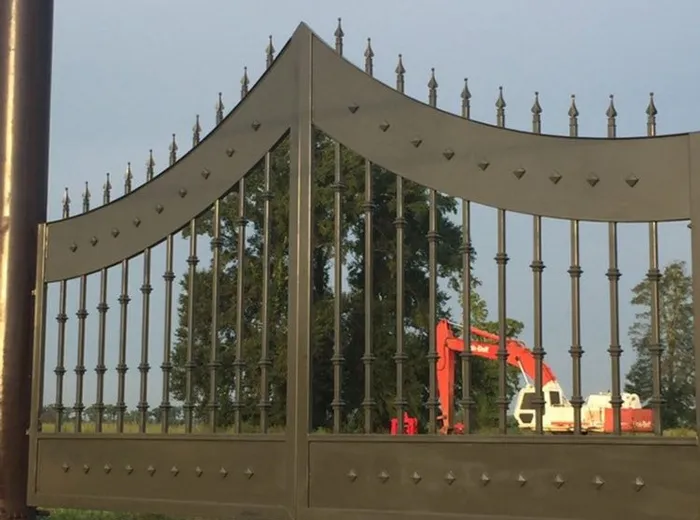 The installed gate seen past its post, with pasture and a parked excavator beyond.