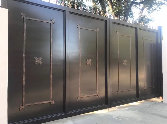The Dallas Estate Gate from the left, the four panels foreshortened along its length and the finials running away above them into sunlight.