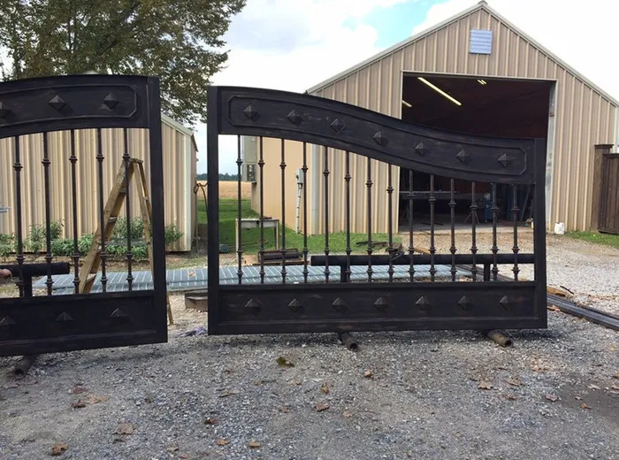 Both leaves standing upright and angled apart on the gravel outside the tan metal workshop, with a farm field and the open barn door behind them.