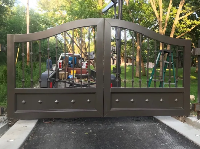 The bronze-brown build closed square across a paved drive under tall trees, a work truck and a stepladder visible through the balusters.