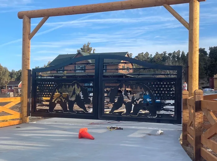 The bear-panel gate from the other side of the drive, closed under its log header with a timber house and cross-buck fencing behind.