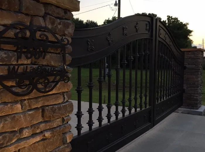The Ham Gate from beside its stacked-stone column, the scrolled iron address plaque set into the stone in the foreground and the fleur-de-lis studs running along the top rail behind it.