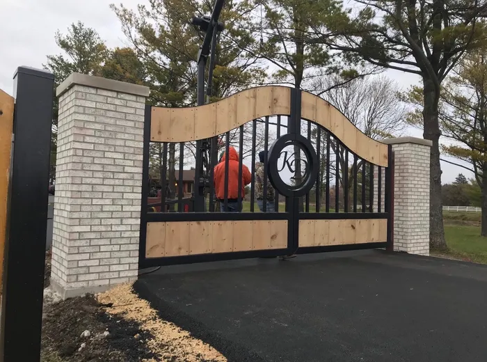 A build hung between white brick pillars on fresh asphalt, boards still pale, with the crew at work behind the closed leaves.
