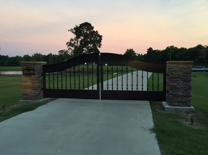 Another twilight view from the drive, both leaves closed and reading as a silhouette between the stone columns, with water lying in the pasture beyond the left column.