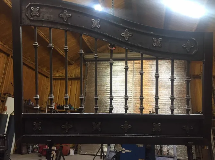 The Ham Gate under fabrication in the shop, one leaf upright on stands showing the curved top rail and rosette-set panels before finishing.