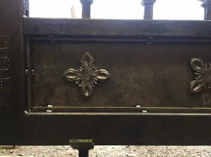 Detail of a cast quatrefoil rosette applied to the gate's solid steel panel, with the dark patina finish visible across the plate.