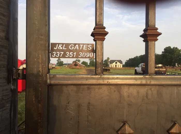 A J&L Gates placard hung in the opening, seen through the balusters with the barn, house and pasture beyond.